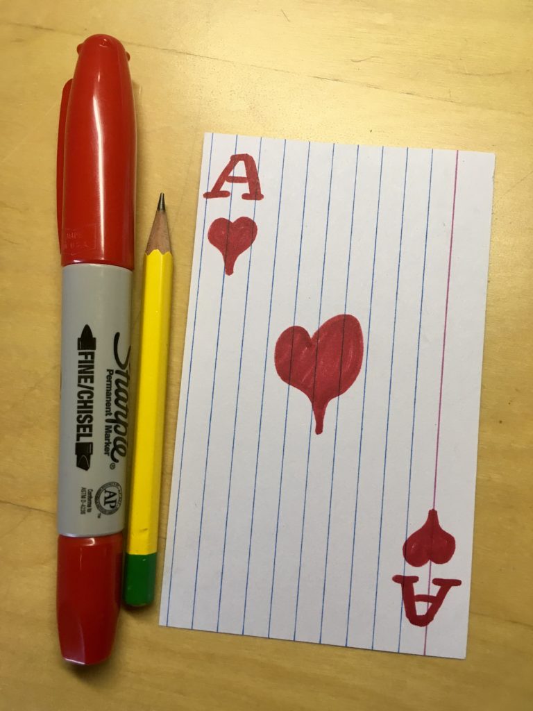 An index card illustrated to look like the Ace of Hearts next to a red marker and pencil.