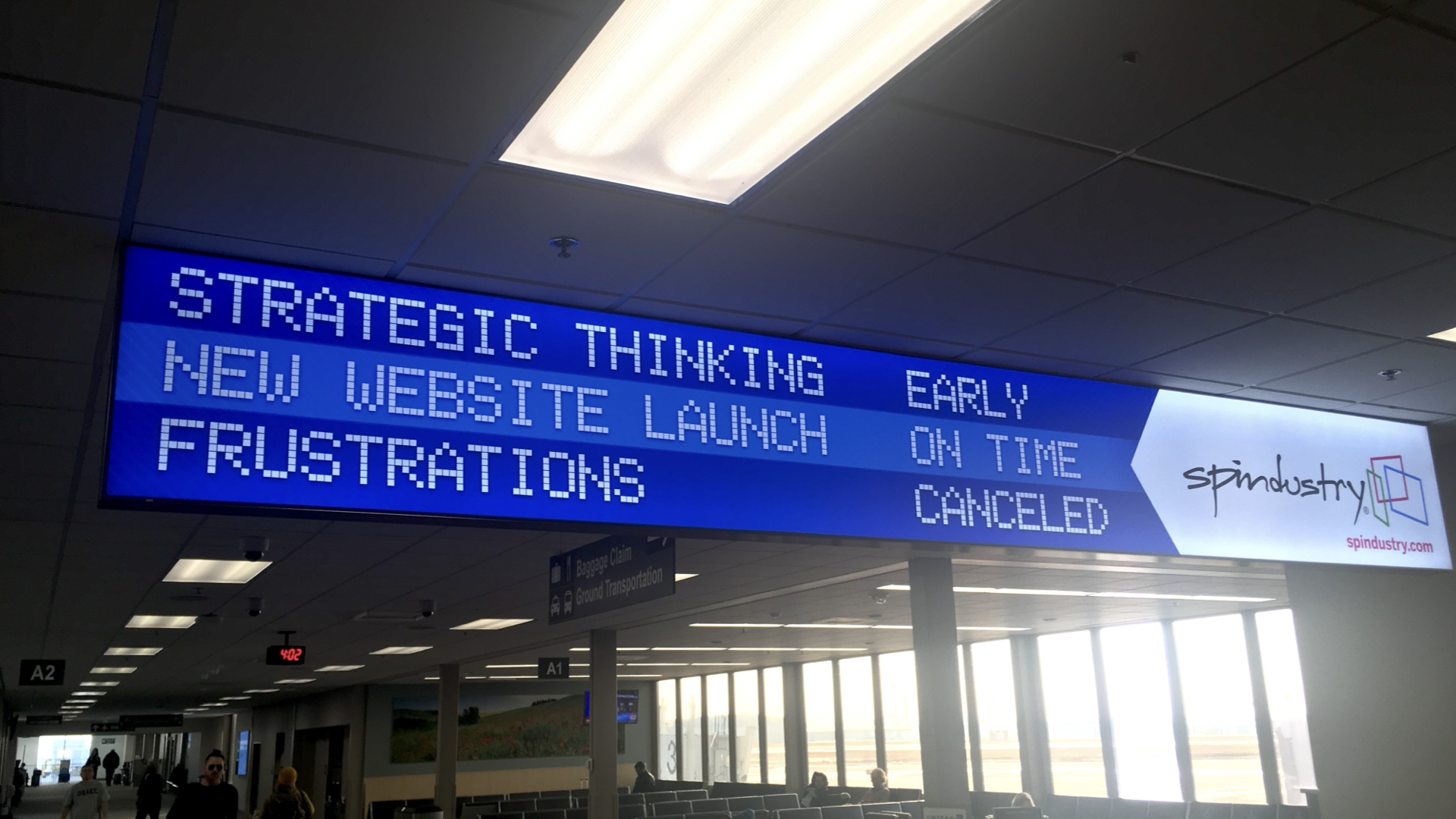 Advertisement in an airport for a company called Spindustry, which mimics a flight arrival/departure display. It includes the phrase "New website launch" marked "On Time"